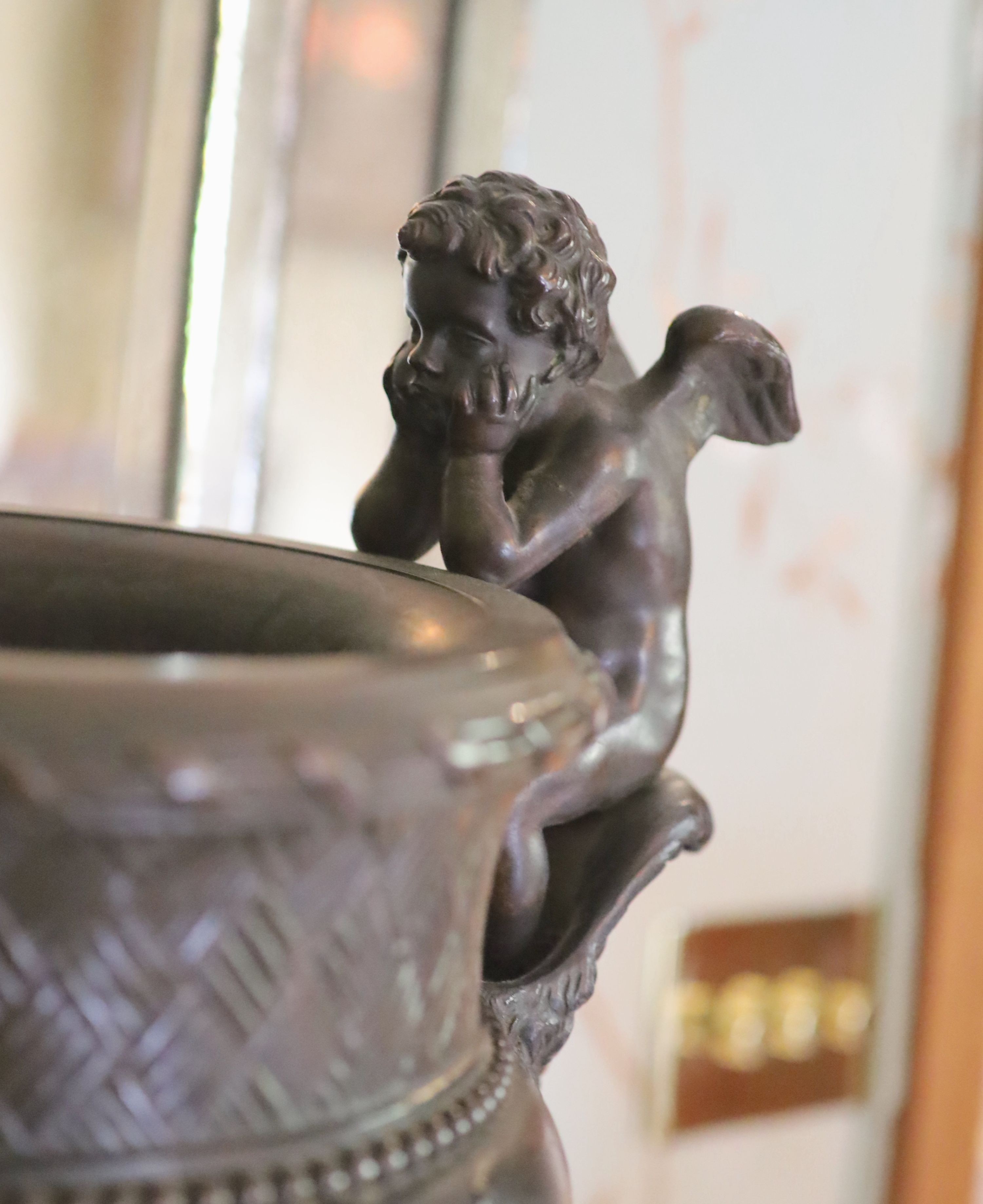 A classical style bronze urn modelled with disconsulate cherubs, height 44cm width 40cm